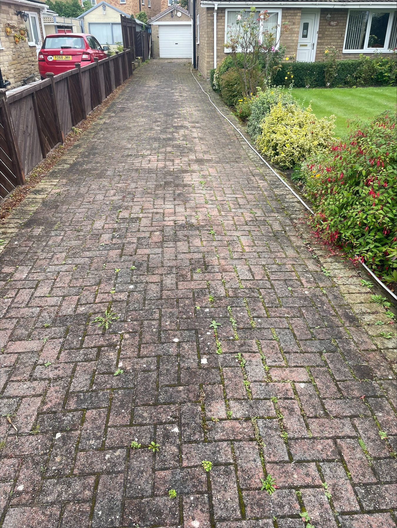 A long block-paved drive beside a garden fence, leading to a garage