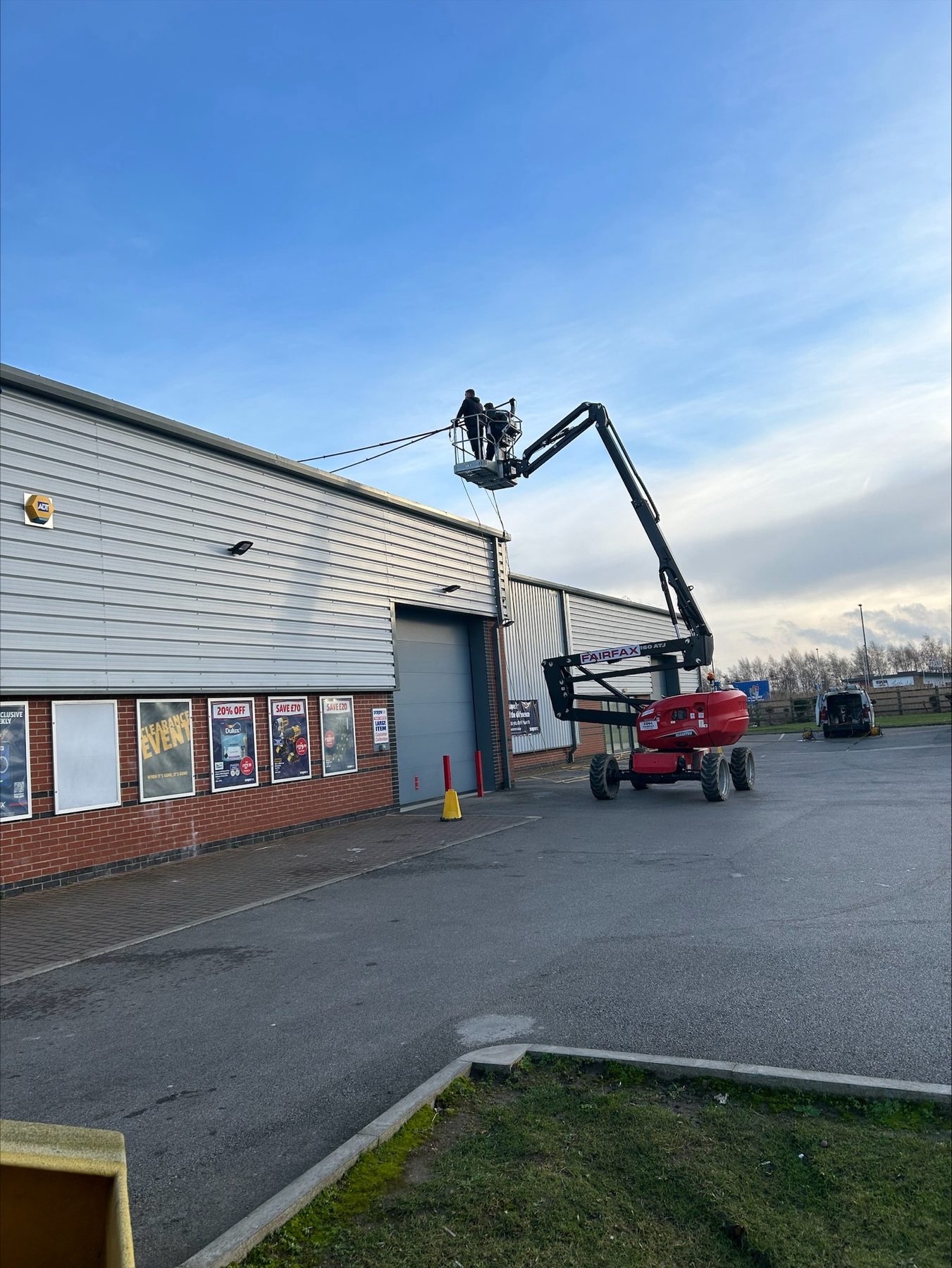 A red cherry picker raised up to the top of an industrial unit under a blue sky