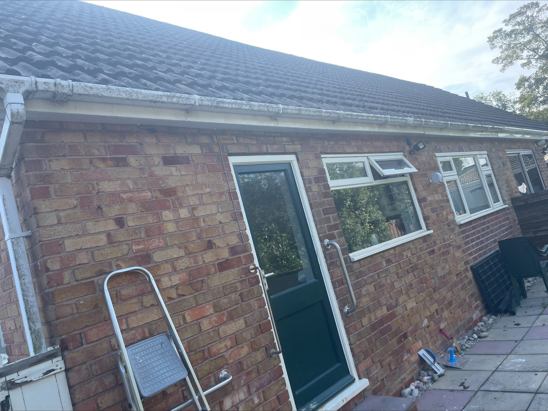 The back of a brick bungalow with white gutters, windows and a green door